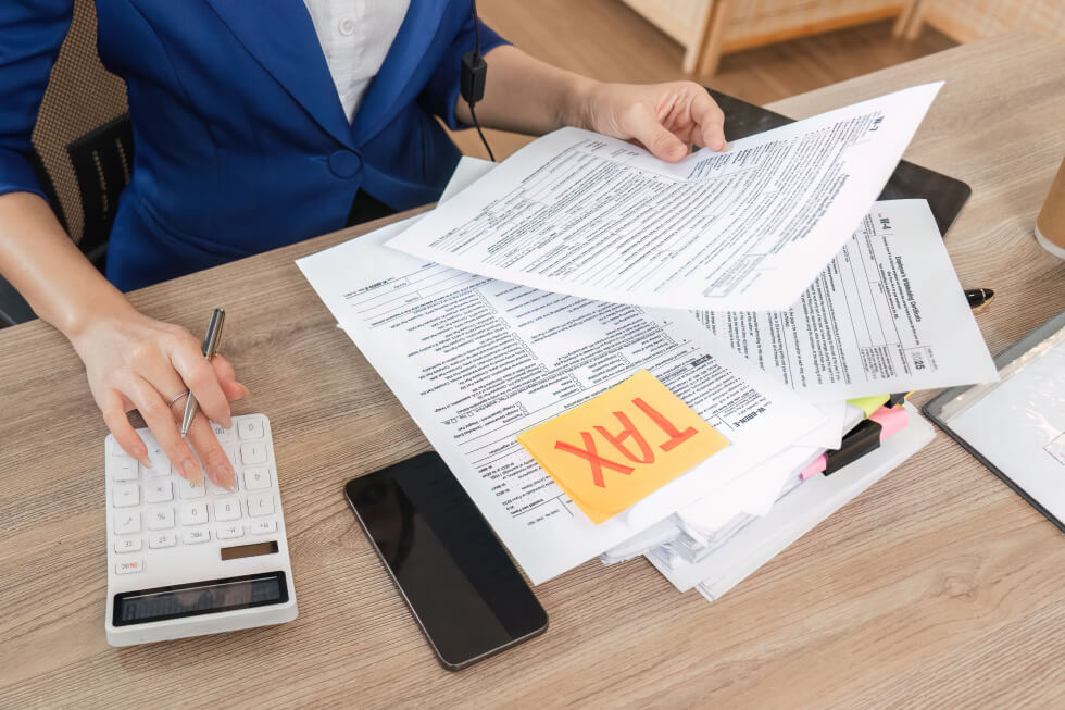 Business professional reviewing tax forms with a calculator and “TAX” note, symbolizing fear and distrust that keep some from hiring a tax strategist.
