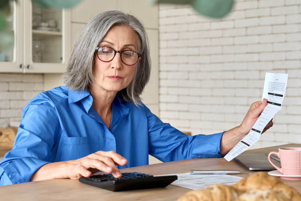 Middle-aged woman using a calculator while scrutinizing a lengthy tax receipt, illustrating the skepticism and mindset blocks that deter some high-income earners from seeking tax-saving advice.